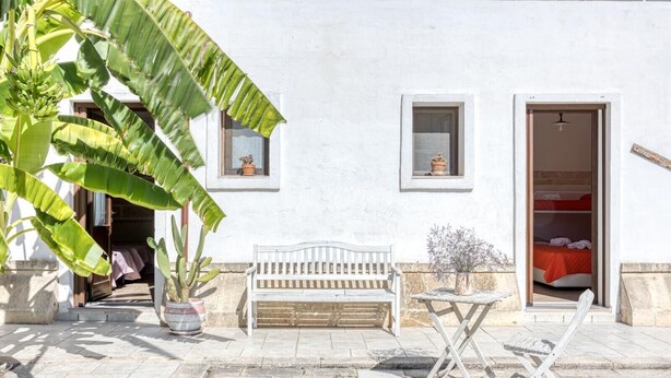 Un bâtiment blanc avec un banc, une table et un pot de fleurs.