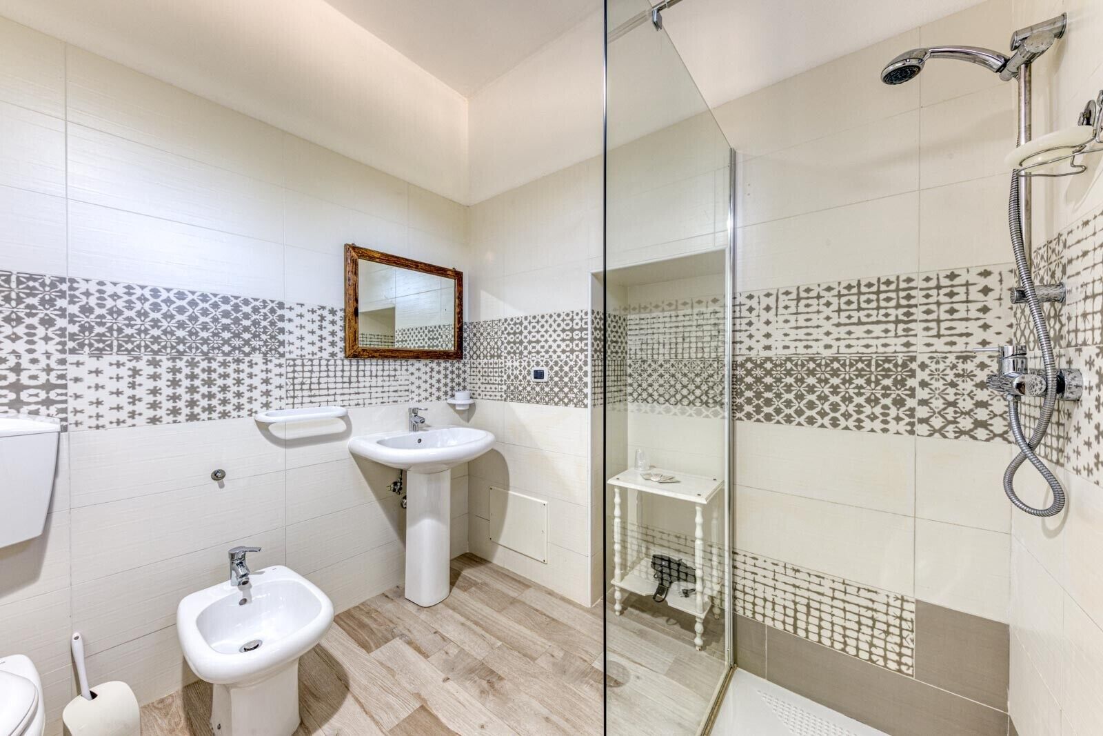 A bathroom with a glass shower enclosure, two sinks, a toilet, and patterned tiles on the walls.