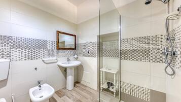 A bathroom with a glass shower enclosure, two sinks, a toilet, and patterned tiles on the walls.