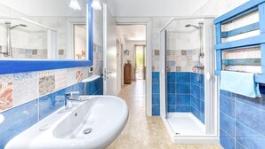 Een badkamer met een witte wastafel, een douche met glazen deur en een betegelde muur met blauwe accenten.