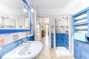 Un bagno con un lavandino bianco, una doccia con porta in vetro e una parete rivestita di piastrelle con dettagli blu.