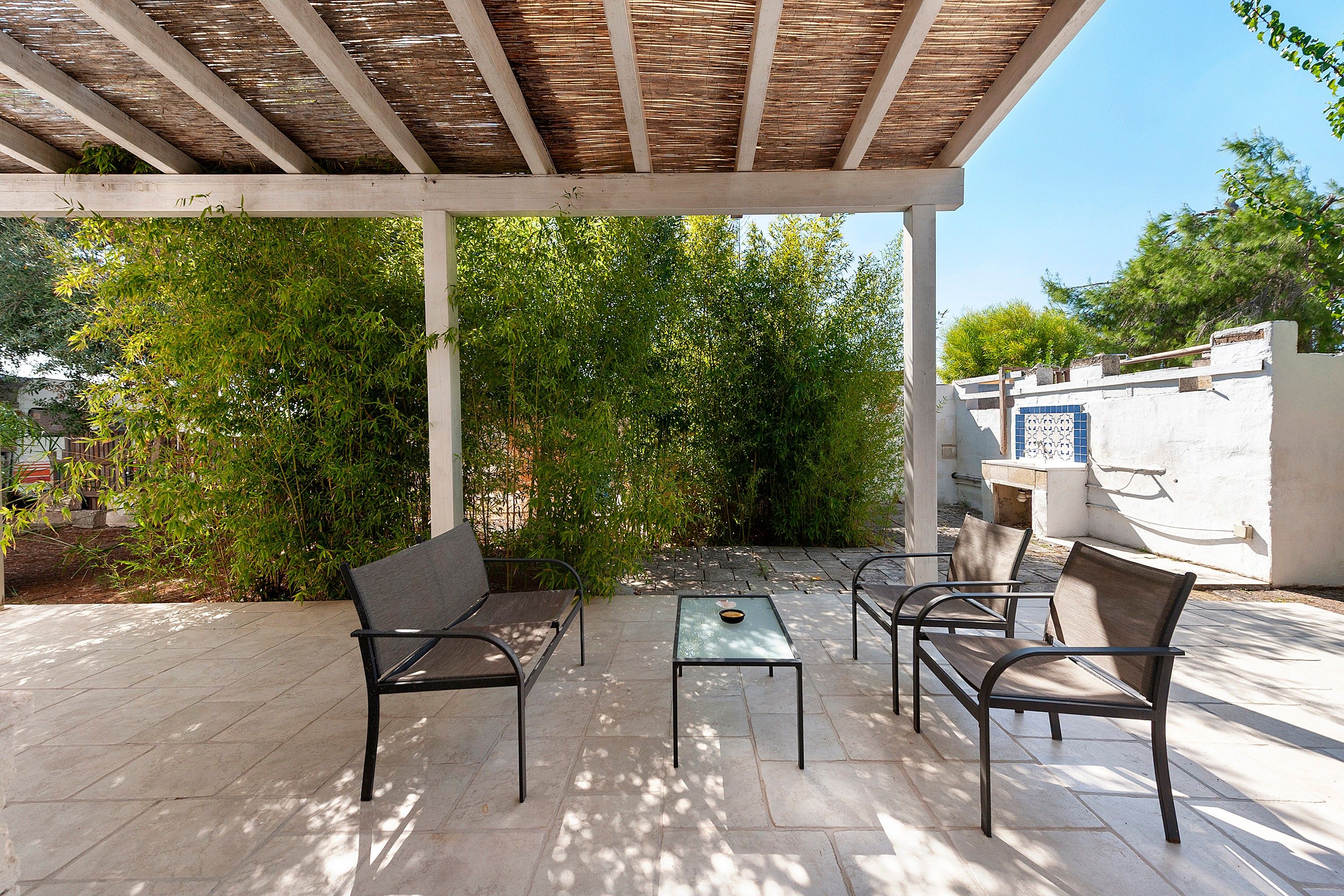 An outdoor patio with a pergola, two chairs, a table, and a small decorative bowl.