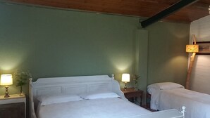 Ein Schlafzimmer mit Holzbalkendecke, einem großen Bett, einem kleineren Bett, zwei Nachttischen mit Lampen und einem gemusterten Teppich.
