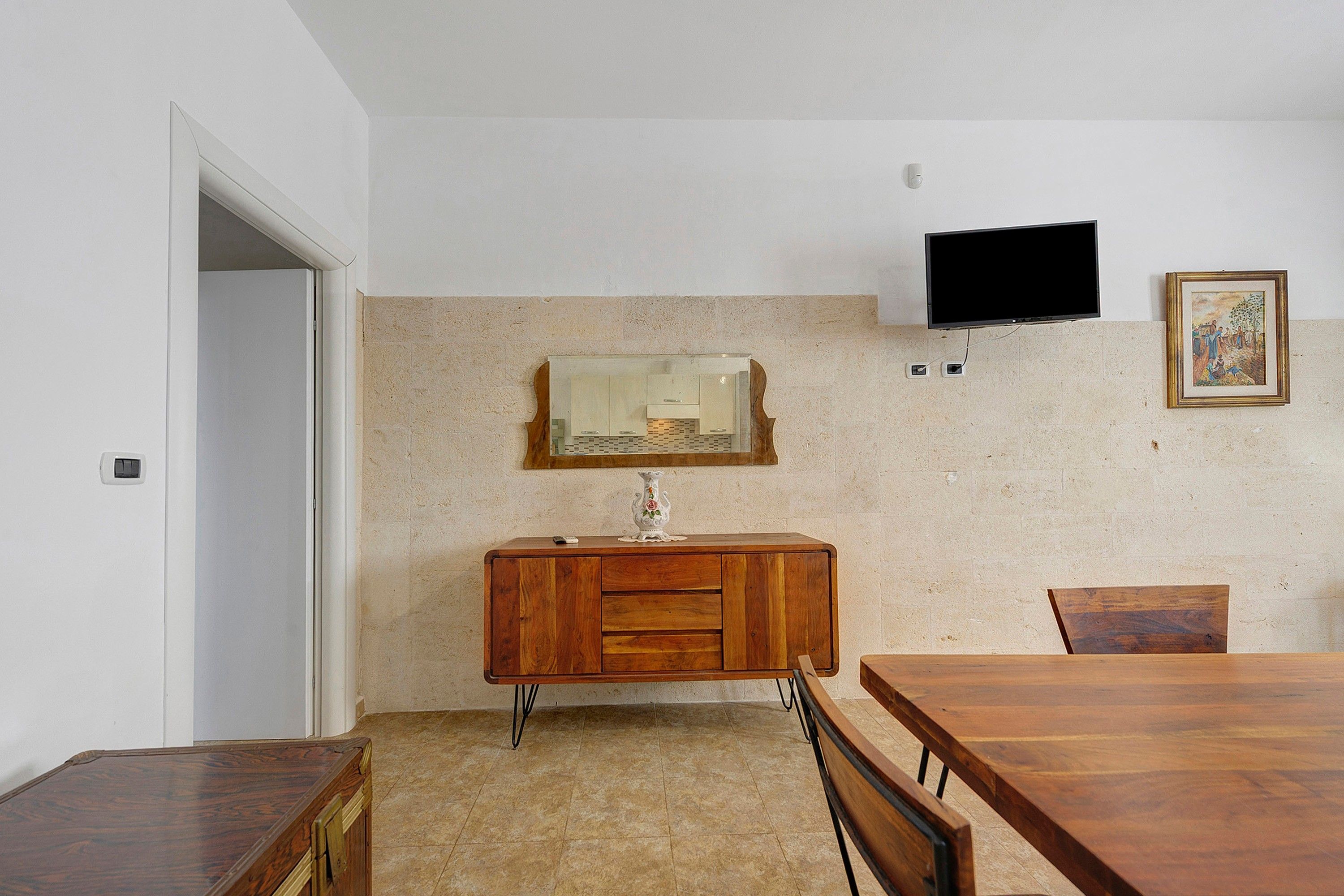 A room with a wooden cabinet, a television mounted on the wall, and a framed picture.