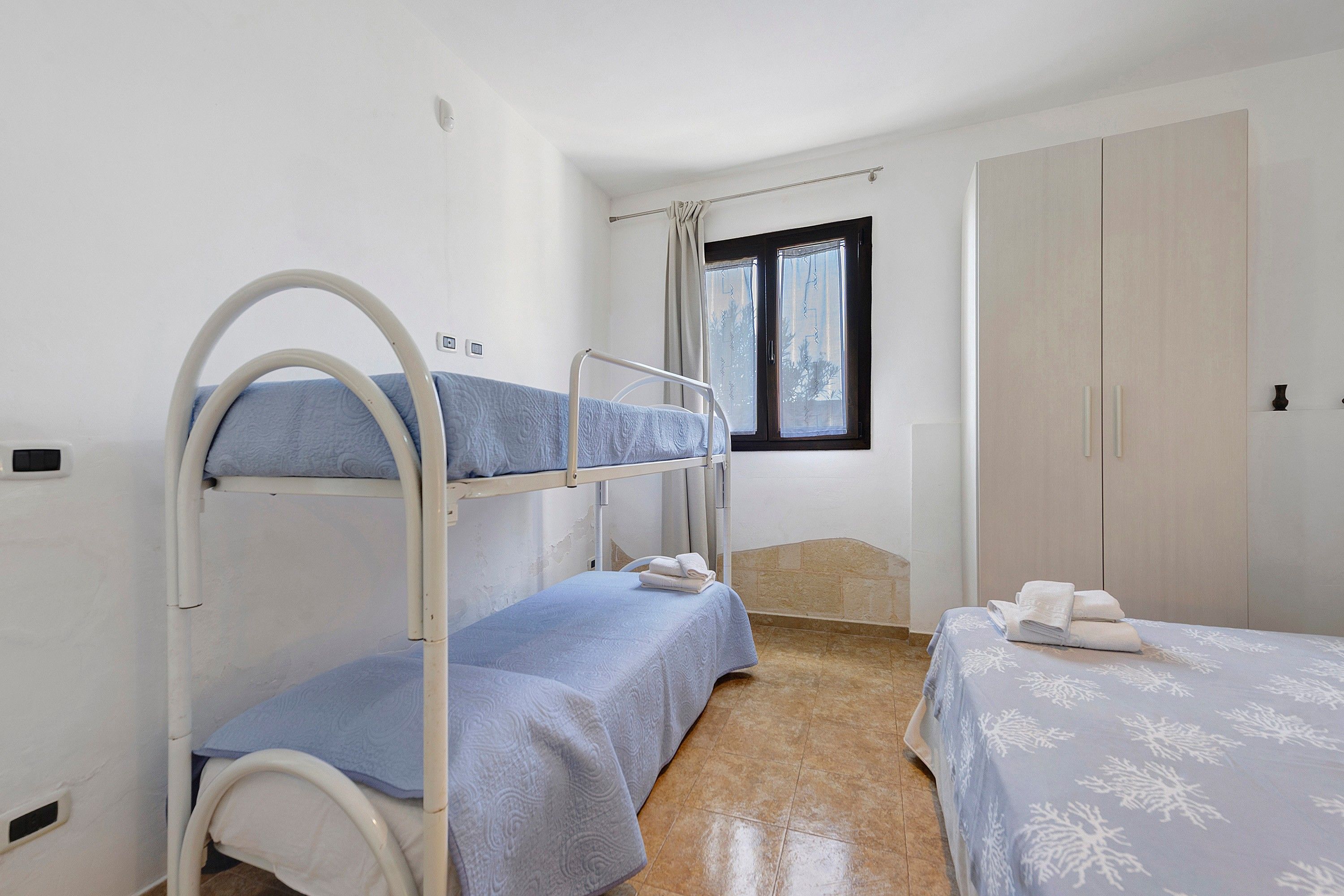 Ein Schlafraum mit Etagenbett, Fenster, Kleiderschrank und einem kleinen Nachttisch.