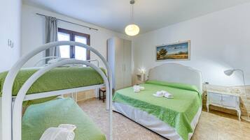 A hotel room with bunk beds, a bedside table with a lamp, a painting on the wall, and a window with curtains.