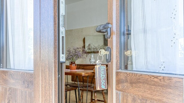 Een open houten deur leidt naar een eetruimte met een tafel en stoelen.