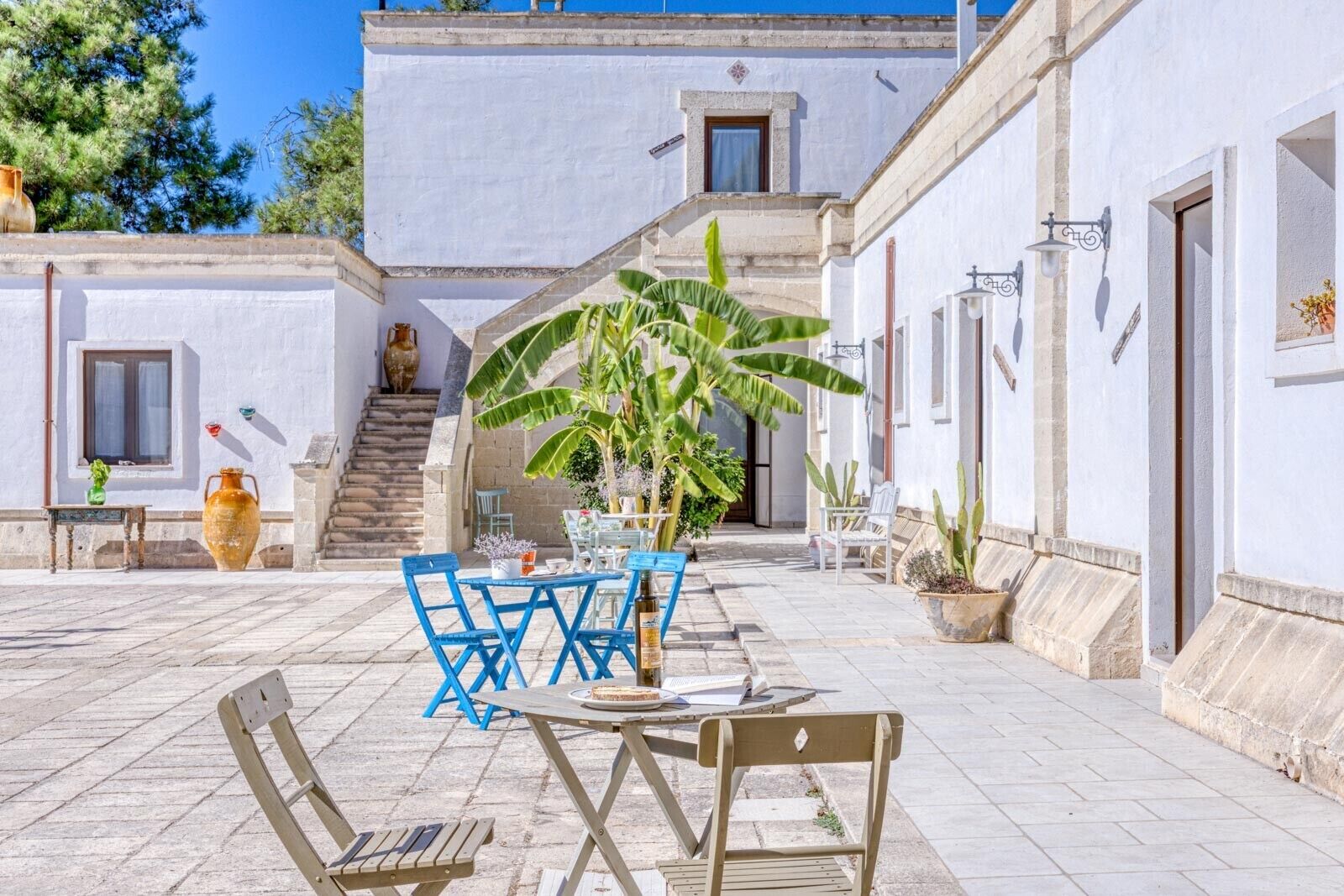 Une cour avec une table et des chaises, un escalier et des plantes en pot.
