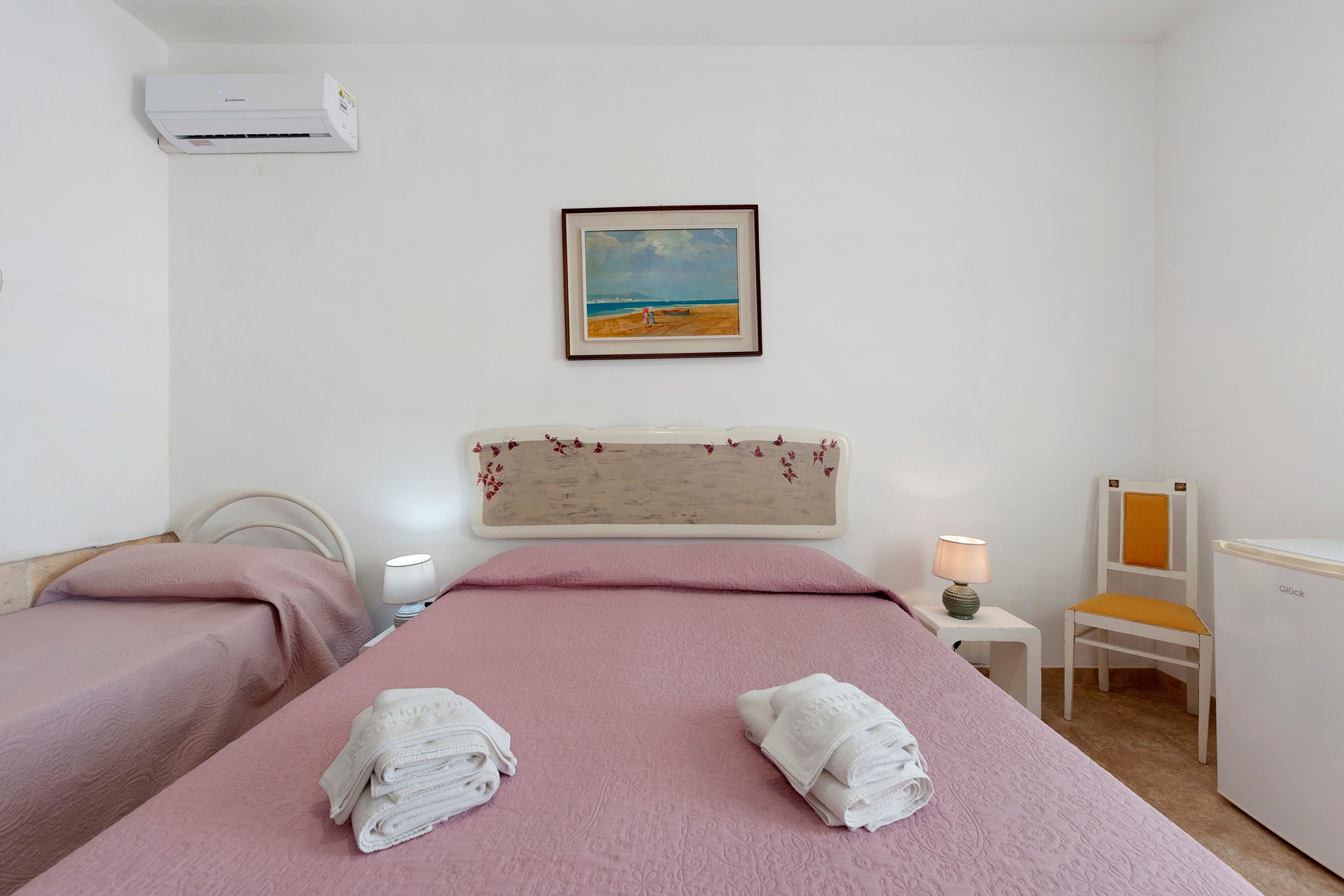 Une chambre d’hôtel avec un lit, une chaise, une table de chevet, une lampe et un tableau au mur.