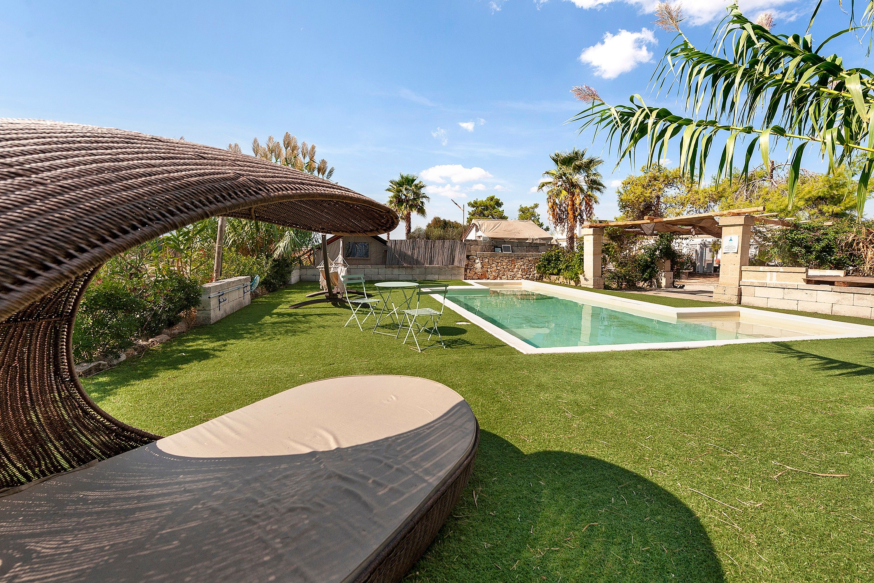 Ein Garten mit Schwimmbecken, einer Lounge-Ecke mit Korbstuhl und einer Pergola.
