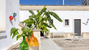 A courtyard with a white building, a bench, a table, and potted plants. - Melograno Room (Porto Cesareo)