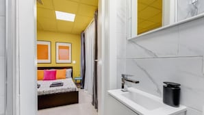 A hotel room with a bed, a bathroom with a sink and mirror, and a view of the hallway.