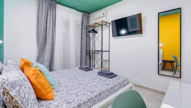 A bedroom with a bed, a TV mounted on the wall, and a mirror reflecting a chair.