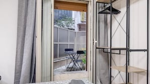 A room with a bed, a small table, a chair, a wardrobe, and a view of the outside.