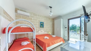 A room with two bunk beds, a desk, a chair, a wardrobe, and a window with a view of the outdoors. - Corbezzolo Room – Ground Floor, 4 Beds, Air Conditioning, Private Bath (Porto Cesareo)