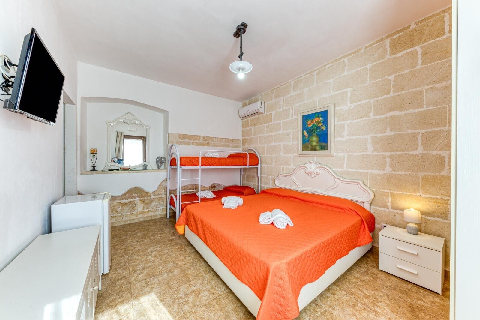 Une chambre avec des lits superposés, un bureau, une télévision et un tableau accroché au mur.