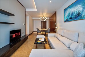 Una sala moderna con televisor de pantalla plana, un sofá, una zona de comedor con sillas y un cuadro en la pared.