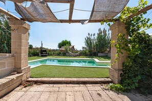 Ein Pool mit Pergola, umgeben von viel Grün und blauem Himmel.