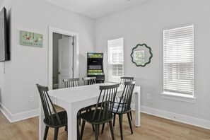 A dining area with a white table and black chairs, a 3D golf game machine, and a framed picture on the wall. - The Golden Tee Pet Friendly 2.5 Blocks to Beach (Myrtle Beach)