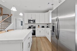 A modern kitchen with white cabinetry, stainless steel appliances, and a wooden staircase. - The Golden Tee Pet Friendly 2.5 Blocks to Beach (Myrtle Beach)
