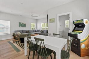 A modern living room with a white table, green chairs, a grey sofa, and a golf arcade game. - The Golden Tee Pet Friendly 2.5 Blocks to Beach (Myrtle Beach)
