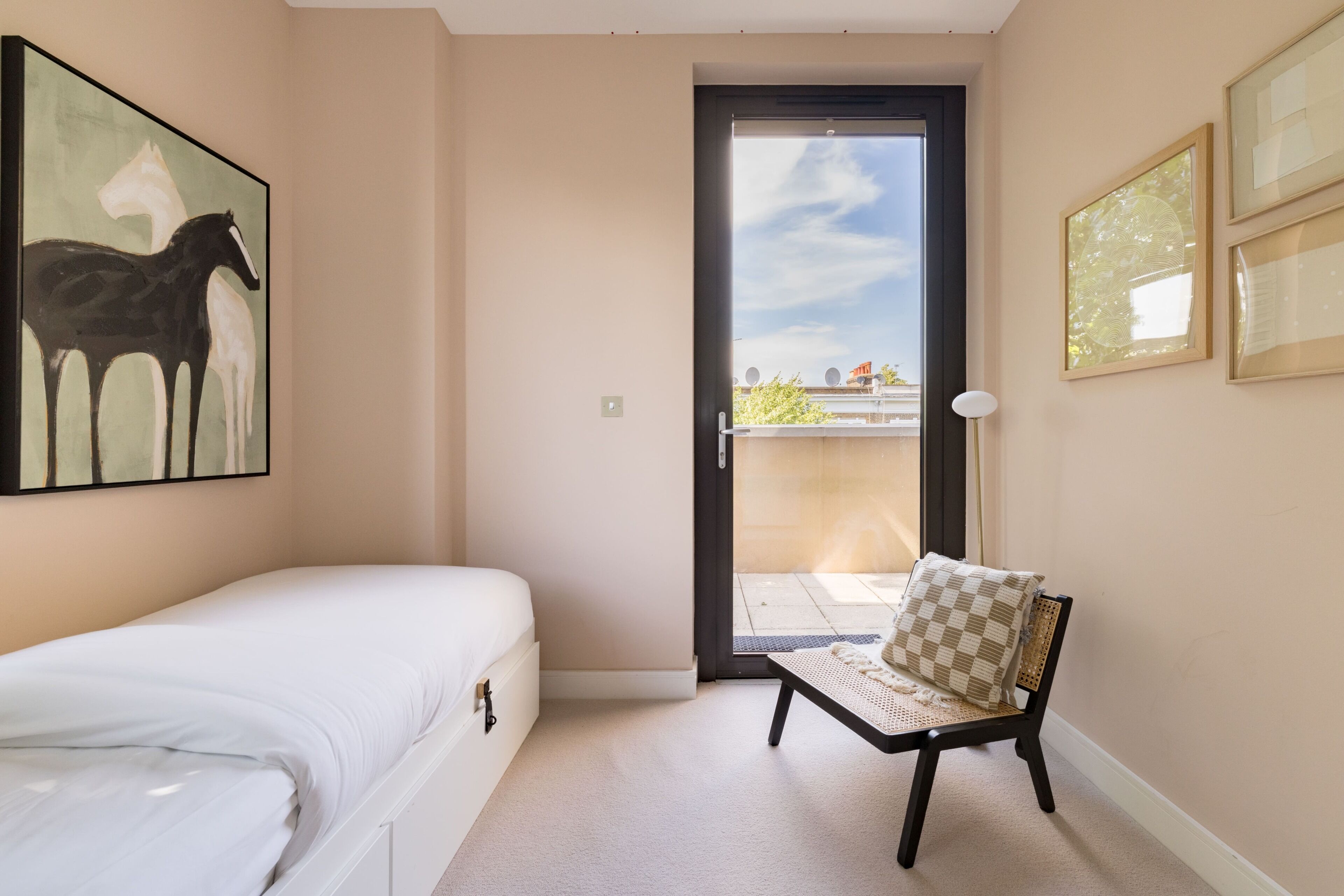 A hotel room with a bed, a chair with a cushion, a door leading to an outdoor area, and a painting on the wall.
