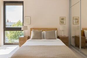 A bedroom with a large window, a bed with white bedding, two bedside tables with lamps, and framed artwork on the wall. - Terrace Light in the Vale (London)