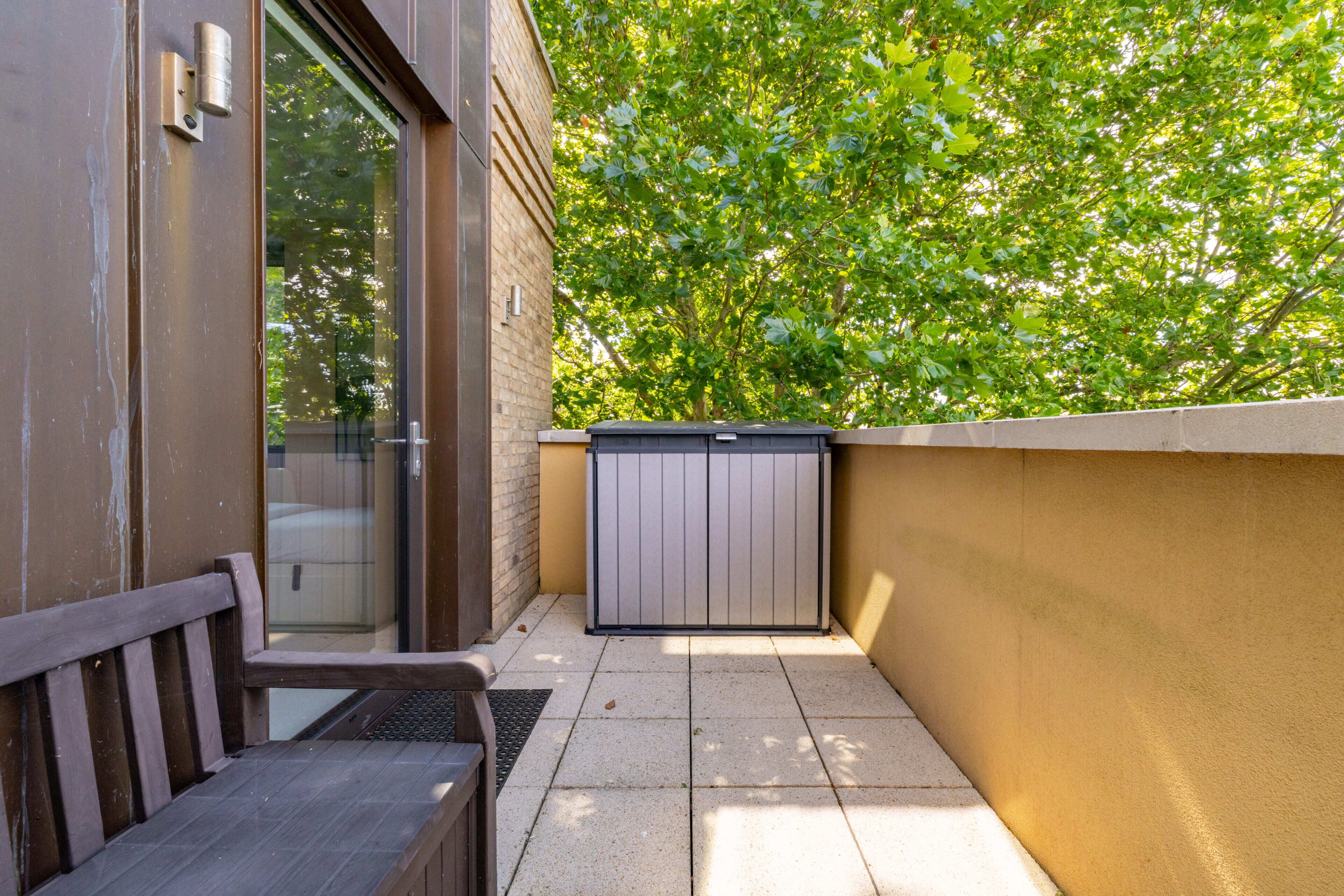 Un petit espace extérieur comprenant un banc, une porte et un luminaire fixé au mur.