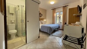 Una habitación de hotel con cama, escritorio, silla, ducha y baño.