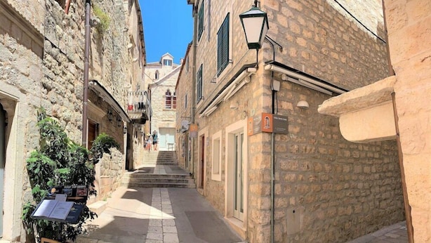 Una calle estrecha con edificios de piedra, un farol y un letrero.