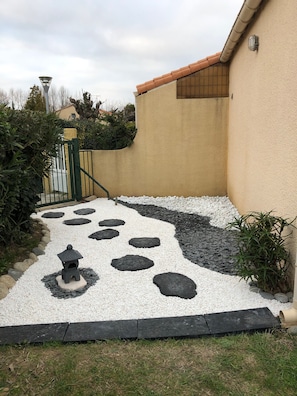 A pathway with stepping stones leading to a gate, surrounded by a low wall and vegetation.