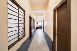 Un pasillo con un extintor montado en la pared, una puerta con placa de número y una ventana con barrotes.