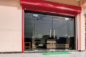 Entrada de un edificio con puerta de vidrio, toldo rojo y felpudo verde en el suelo.