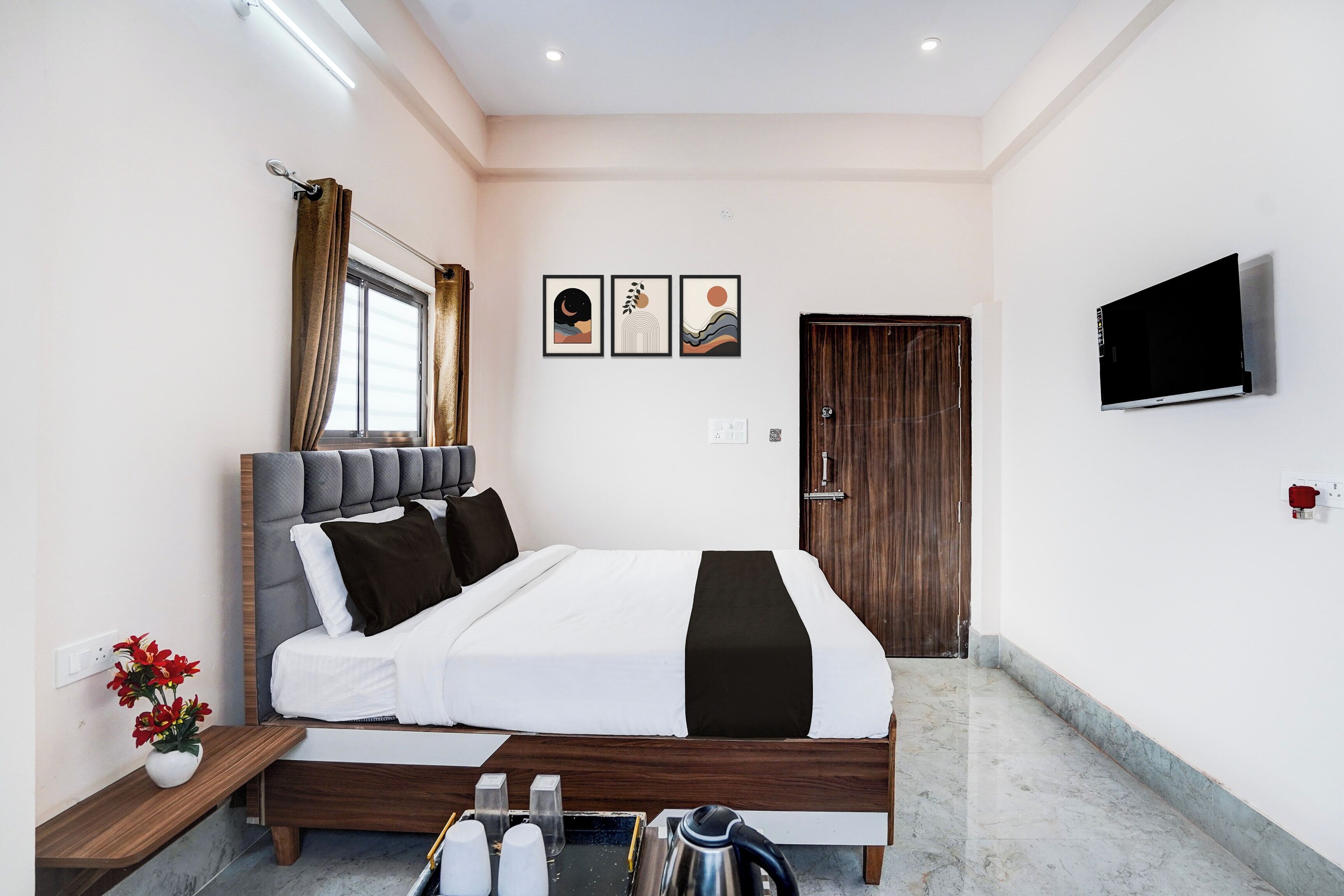 Une chambre à coucher moderne avec un lit, une table de chevet, un téléviseur, une œuvre d’art et une porte.
