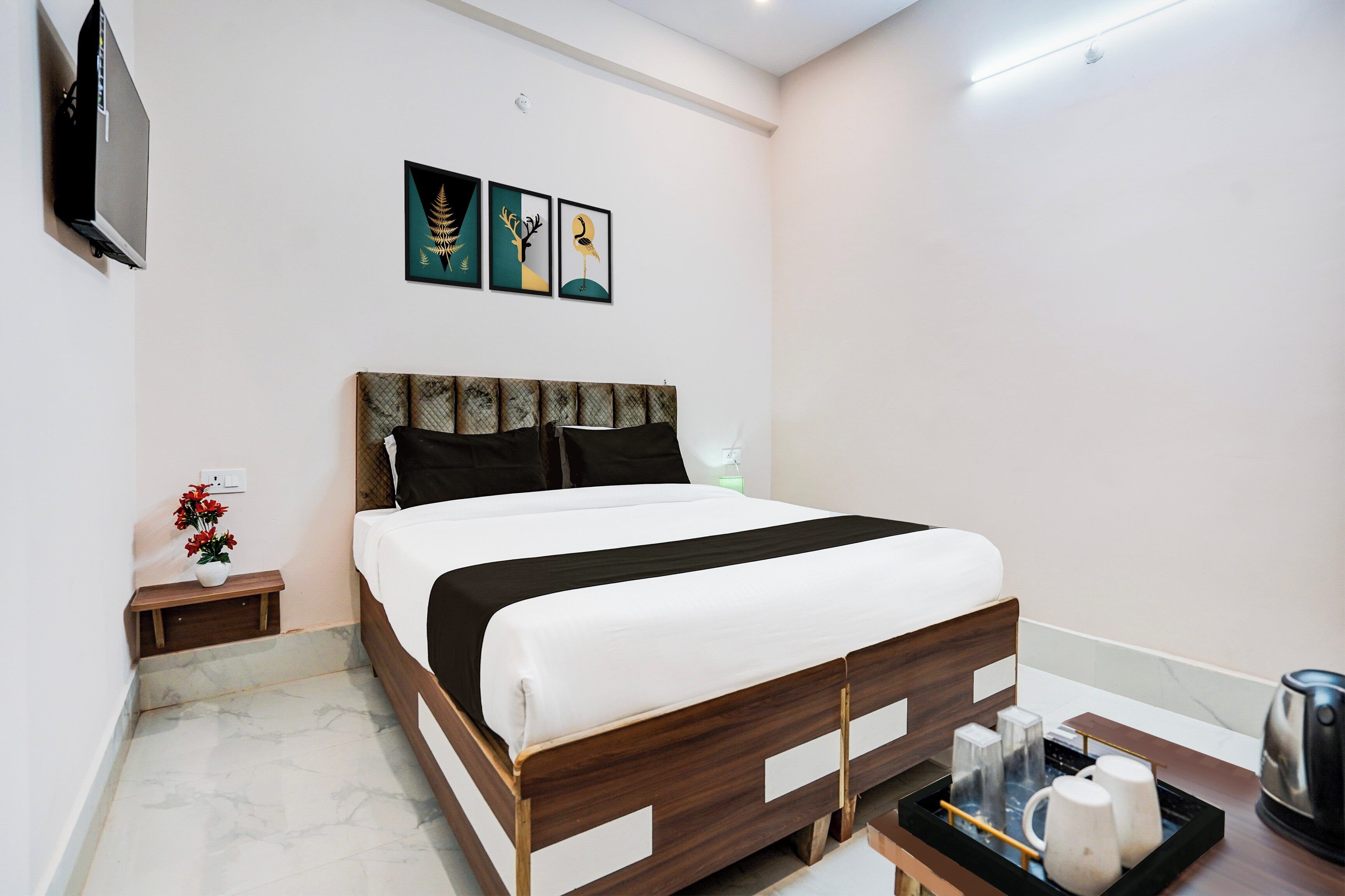 Une chambre d’hôtel comprenant un lit, une table de chevet, un téléviseur fixé au mur et trois œuvres d’art encadrées.