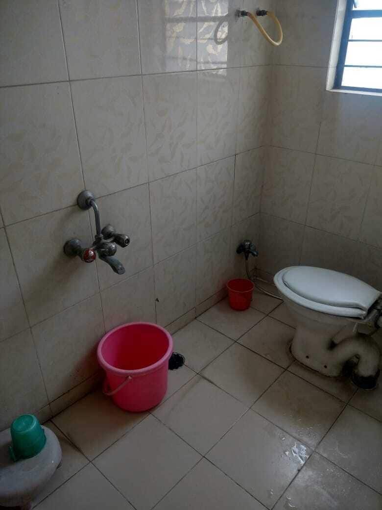 Un baño pequeño con inodoro, ducha y lavamanos. Hay un cubo rojo en el suelo.