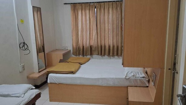 A room with a bed, a bedside table, a chair, a wardrobe, and a small rug. - Hotel Rahi (Nashik)