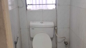 A small, compact bathroom with a toilet, a sink, and a shower. - Hotel Rahi (Nashik)