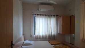 A room with a bed, a ceiling fan, an air conditioning unit, a window with curtains, and a wardrobe. - Hotel Rahi (Nashik)