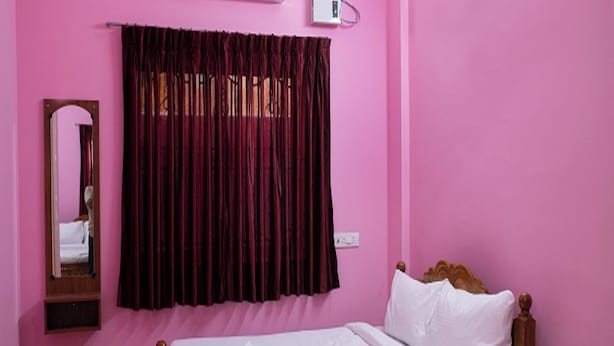 A room with a bed, a mirror, a window with curtains, and an air conditioning unit. - Sri Siva Shankara Inn (Tiruvannamalai)