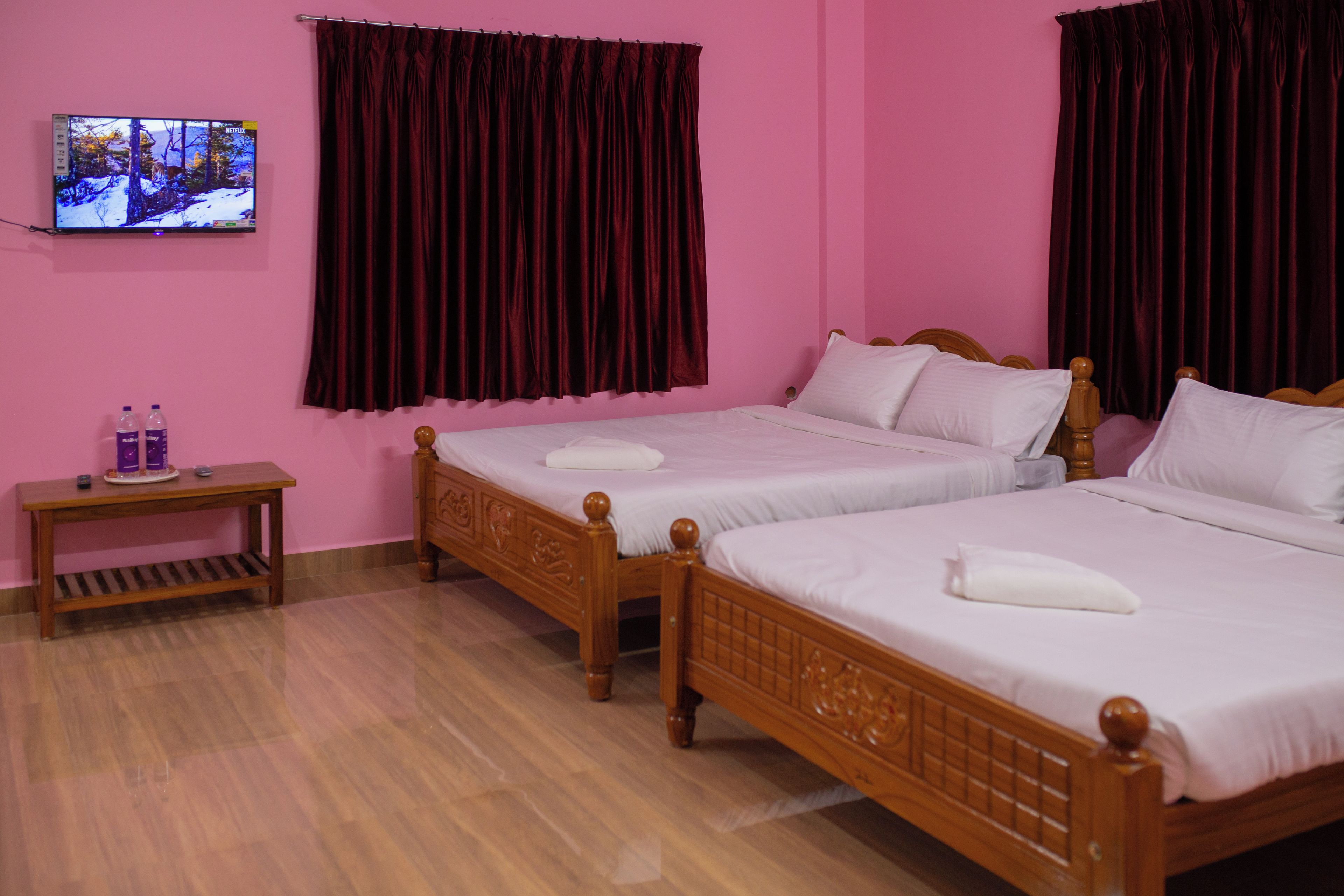 A hotel room with two wooden beds, a wooden nightstand, a television on the wall, and a pink wall.