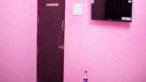 A room with a closed door, a small table with a bottle, and a wall-mounted television. - Sri Siva Shankara Inn (Tiruvannamalai)