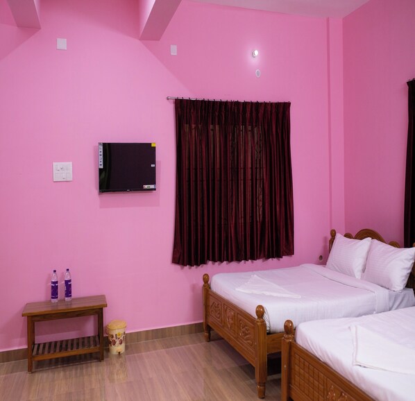 A pink room with a bed, a TV, a curtain, a small table, and a trash bin.