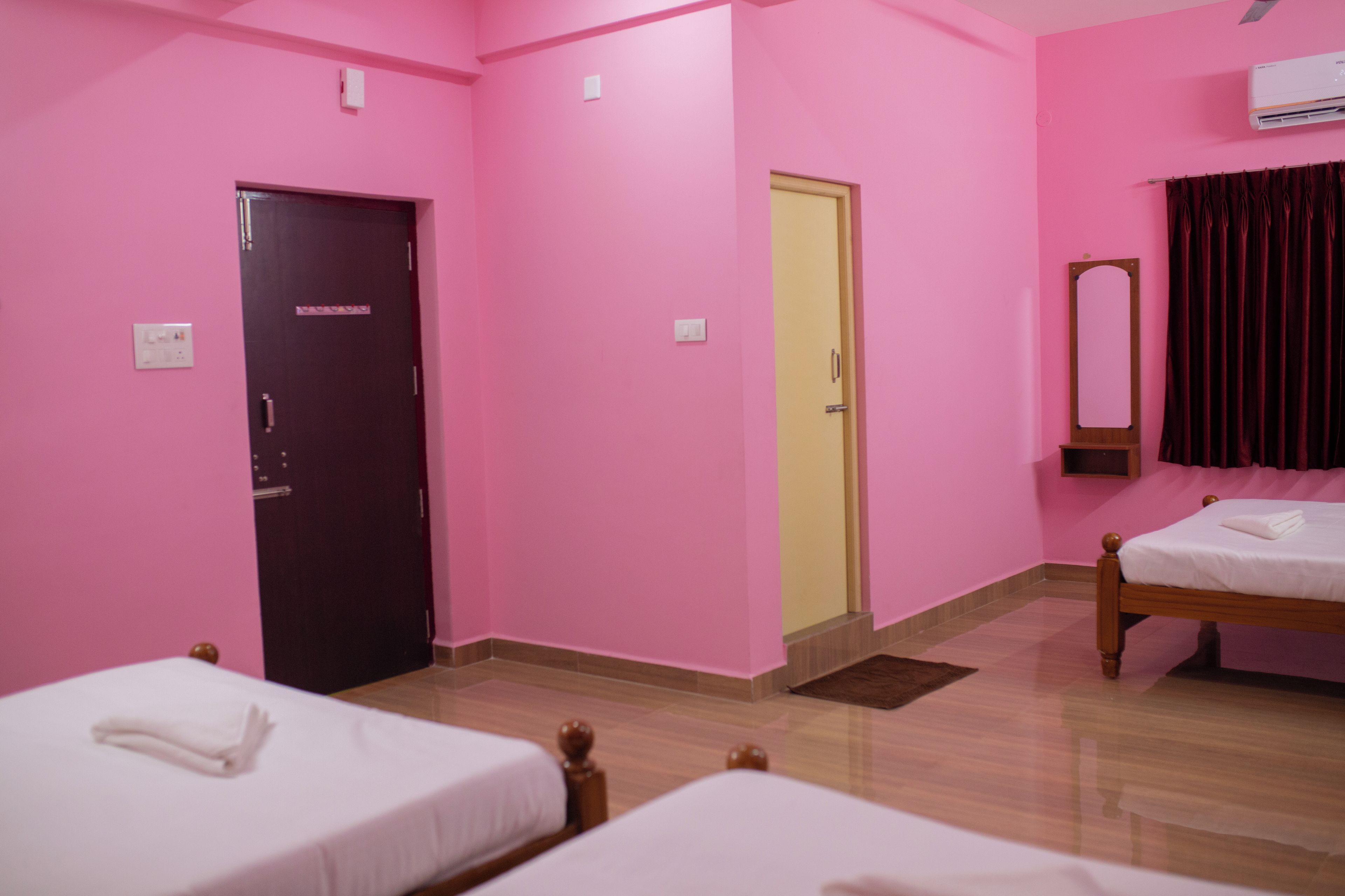 Una habitación con paredes rosas, dos camas, una puerta y un espejo.