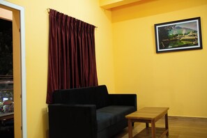 Una habitación con un sofá oscuro, una mesita de madera y una pared amarilla.