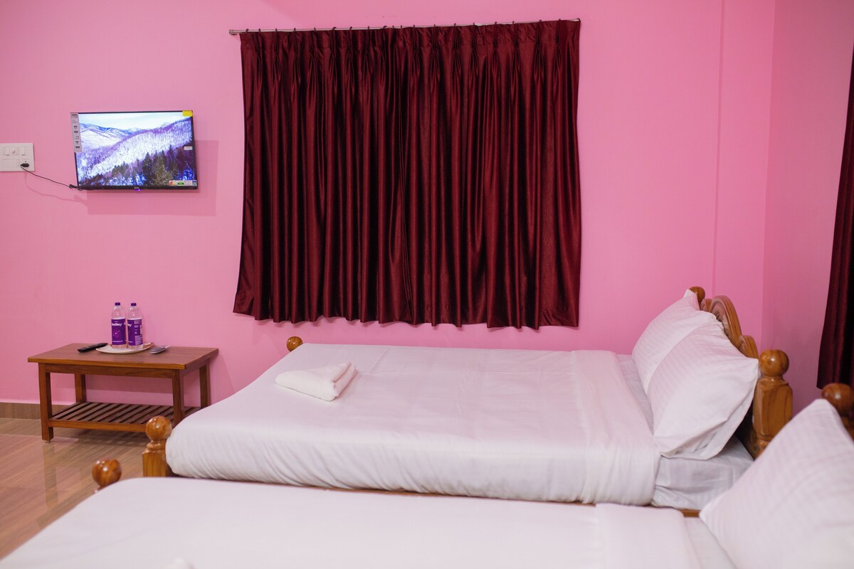 A hotel room with a bed, a TV mounted on the wall, a small table with a remote control, and a bottle of water.