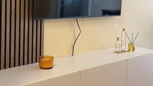 A flat-screen TV mounted on a wall above a white cabinet with a candle and reed diffuser on it. - Green Pine Studio Hils Brauner - Free Parking - Nearby Metro Station (București)