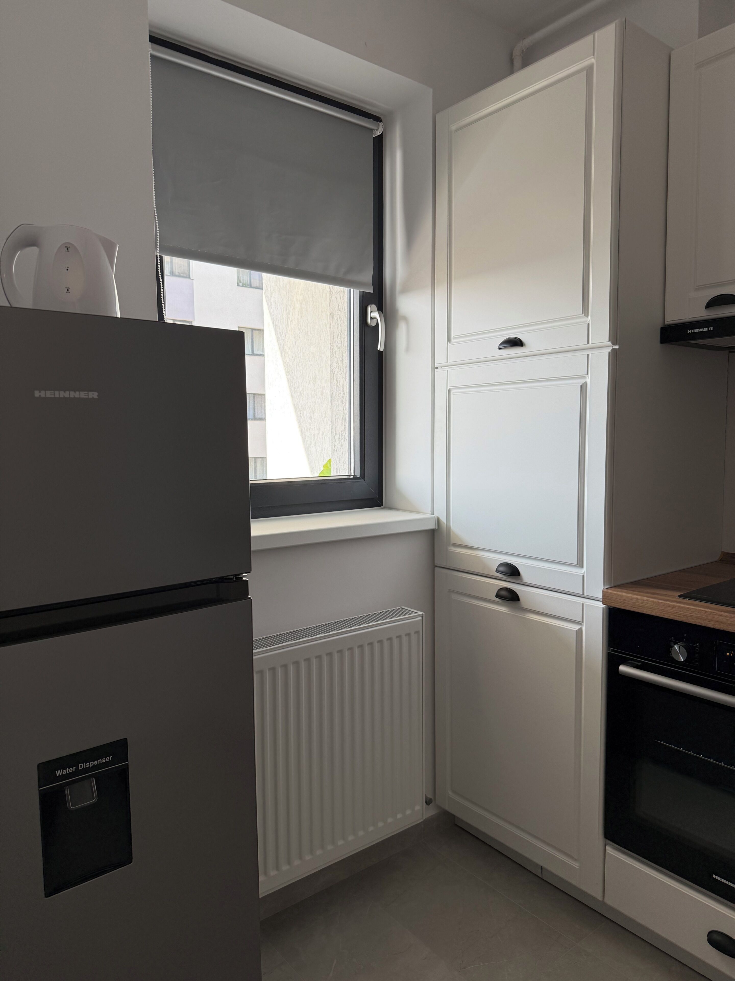 A kitchen with a built-in water dispenser, a window with a blind, and a stove.