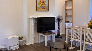 Una sala de estar con televisor, ventilador, sofá, mesa de centro y lámpara de araña.