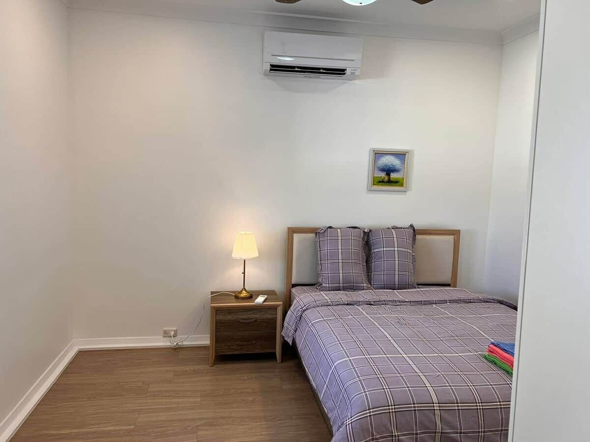 A bedroom with a bed, a nightstand with a lamp, and an air conditioning unit on the wall.